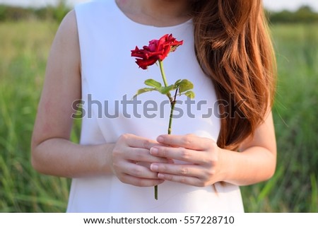 The woman is holding the rose with grass field background in Thailand