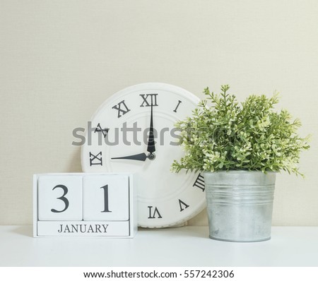 White wooden calendar with black 31 january word with clock and plant on white wood desk and cream wallpaper textured background , selective focus at the calendar