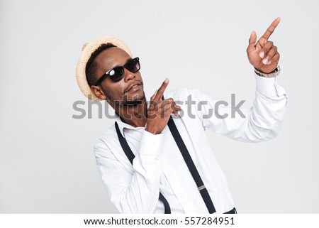 Picture of attractive african man wearing hat posing in studio while pointing. Isolated over white background. Look aside.
