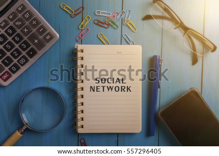   Top view of SOCIAL NETWORK written on the notebook,magnifier glass,calculator,smart phone,pen and glasses on blue wooden desk.business concept.