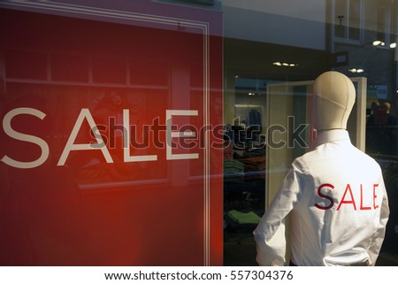 male fashion doll with sale printed on white shirts in shop window and sale sign on wall