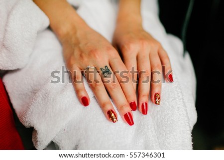 Women's hands with a red manicure and tattoo