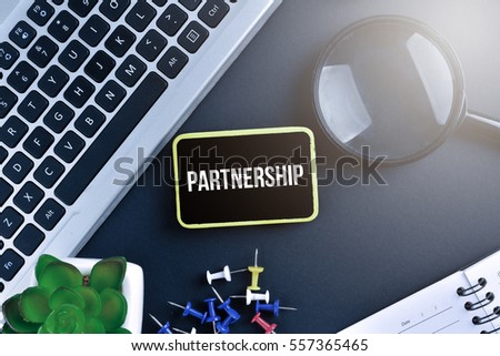 Keyboard with magnifying glass on black background with text PARTNERSHIP
