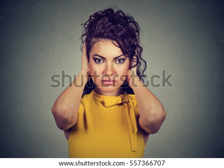 Young attractive woman covering with hands her ears looking at camera isolated on gray wall background. Hear no evil concept 