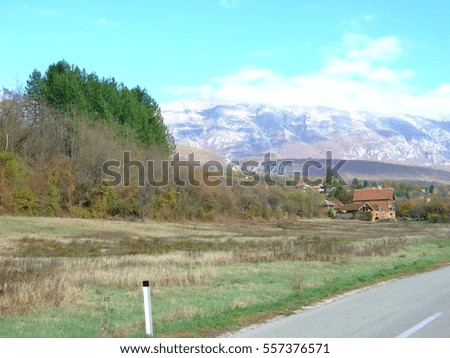 Early autumn landscape in Europe. Trees around the hill side meadow and a mountain ridge in the distance. Beautiful mountains landscape and blue sky.