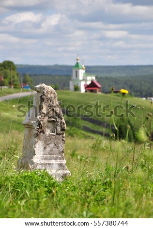 abandoned anonymous headstone in the field on the background of rural landscape with village church