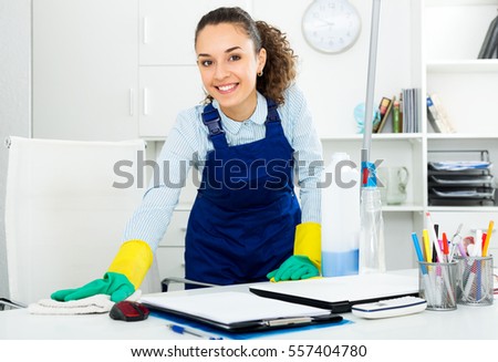Pretty woman in uniform with supplies cleaning in office Royalty-Free Stock Photo #557404780