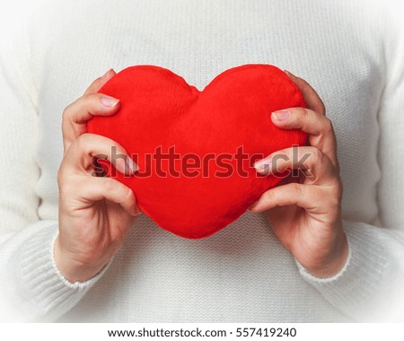 Young woman in white knitted sweater holding in hands red soft heart shape. Symbol of love. Valentines day concept. Toned picture.