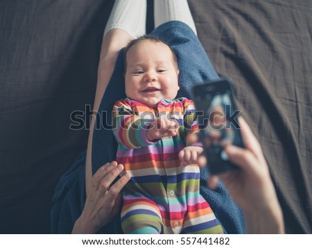 A mother is using her smartphone to take a photo of her baby