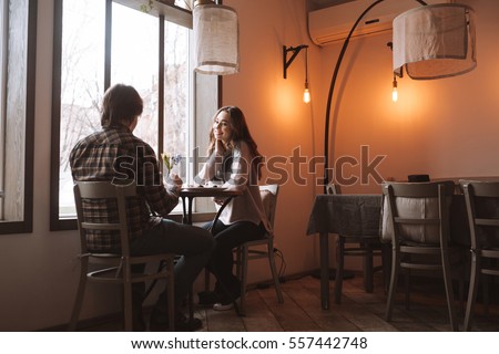 Picture of loving happy couple sitting at the table in cafe near window while looking at each other.
