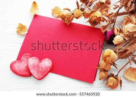 Decorative red hearts, blank red card with space for text and dry roses on a white surface, close up. Romantic image, gift by St. Valentine's Day.