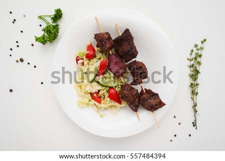 Appetizing shashlik with salad on plate flat lay. Top view on grilled pork sticks served with fresh vegetables. Healthy food, dinner, menu concept