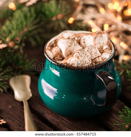 Enamel cup of hot cocoa with marshmallows on rustic wooden background with beautiful Christmas lights of bokeh. Christmas concept