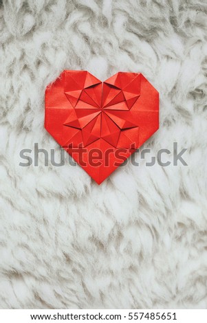Red paper folded origami handmade heart on white natural fluffy fur background. Valentines day cozy vertical postcard template. Empty space for text, copy, lettering.