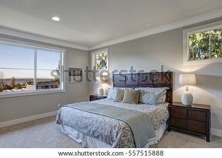 Gray bedroom design with queen size bed accented with high wood headboard and dark wood nightstands with lamps. Northwest, USA