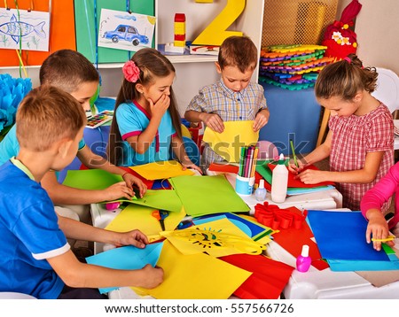 Child cutting paper in class. Kids development and social lerning children in school. Children's project in kindergarten. Pictures into background