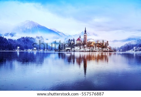 Winter landscape Bled Lake. Travel Slovenia, Europe. Bled Lake one of most amazing tourist attractions. View on snowy Island with Catholic Church in Bled Lake with Castle and Alps in Background. Royalty-Free Stock Photo #557576887