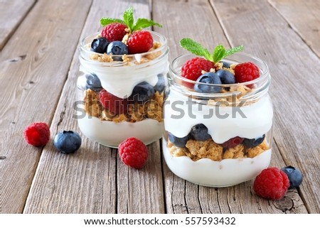 Healthy blueberry and raspberry parfaits in mason jars on a rustic wood background