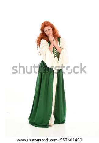 full length portrait of a curly, red haired woman wearing green medieval gown. standing pose, isolated against a white studio background.