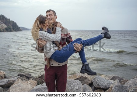 Happy thoughtful couple standing on a rock beach near sea hugging each other in cold foggy cloudy autumn weather. Copy space