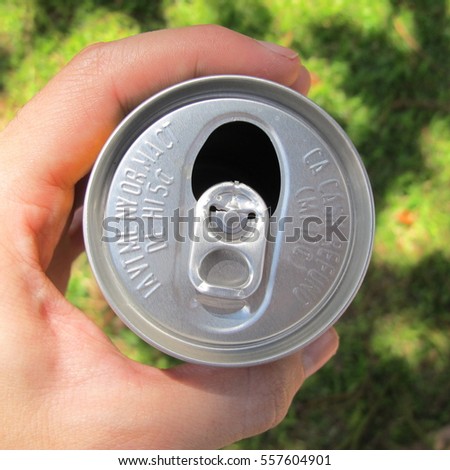 Drinking concept. Top view of a hand holding an opened soda can, grass at background