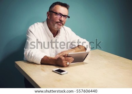 Portrait of skilled male business coach checking online projects of his students reading their reports via modern touchpad and wireless connection to internet sitting on copy space for advertising