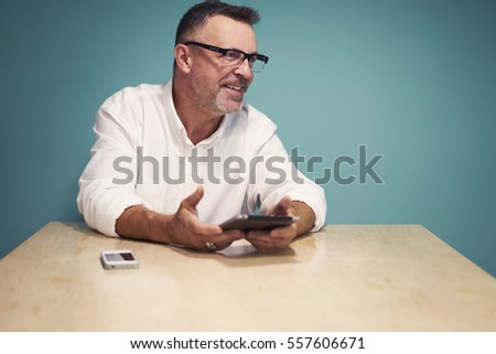 Experienced successful handsome male blogger holding gadget connected to internet while monitoring online news and making press release for popular web page sitting on copy space for your advertising