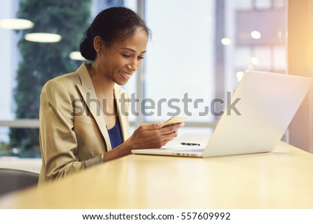 Portrait of smiling afro american female blogger sharing multimedia files with followers waiting for feedback via modern smartphone connected to wifi sitting near copy space for your advertising 