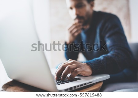 Attractive bearded African man using laptop while sitting on sofa at his modern home office.Concept of young people enjoying mobile devices.Closeup with a focus on male hand.Blurred background Royalty-Free Stock Photo #557615488