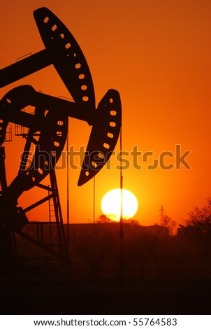 An oil pump jack is silhouetted by the setting sun