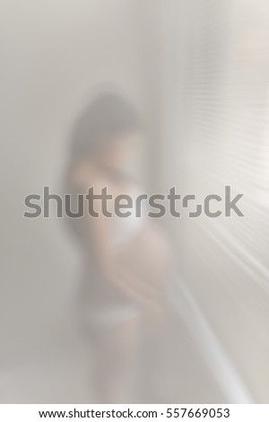 Blurred image of a young pregnant lady standing in front of an window