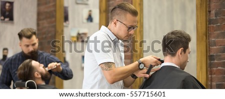 Interior shot of working process in barbershop. Young men getting trendy haircuts in modern barbershop. Cool male hairstylists serving clients. Horizontal photo banner for website header design