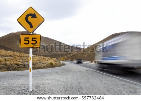 The sign posts of speed limit of 55 kilometer per hour and reverse curve with decreasing radius to the right, with motion-blurred lorry and car