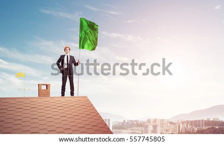 Businessman standing on house roof and holding flag. Mixed media