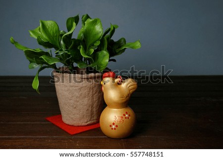 Chinese gold rooster and a green plant on a rustic wooden background. Chinese text means lucky, wealth and prosperity. Chinese New Year concept.