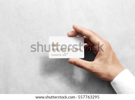 Hand holding blank white credit card mockup with chip and embossed gold info. Plain plastic bank-card display front, design mock up. Electronic money holder template. Royalty-Free Stock Photo #557763295