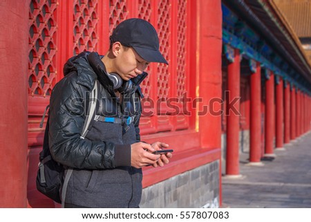 Young Asian traveler with a backpack holding cellphone resting in front of an red ancient Chinese building