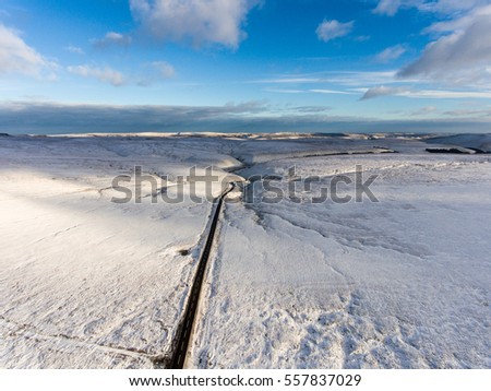 Beautiful aerial view of road going over snowy hills in England.