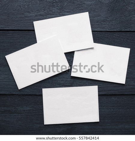 A square photo of blank white thick cardboard business cards on a dark wooden background texture. A mockup or a minimalist banner with copyspace
