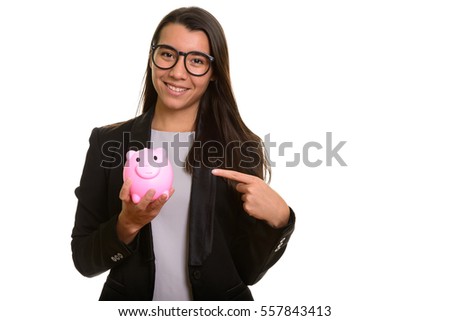 Young happy Caucasian businesswoman smiling and holding piggy bank while pointing finger isolated against white background