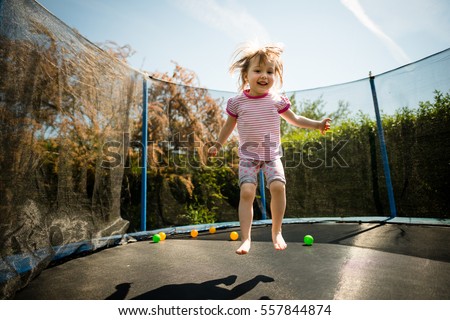 Little child jumping on big trampoline - outdoor in backyard Royalty-Free Stock Photo #557844874