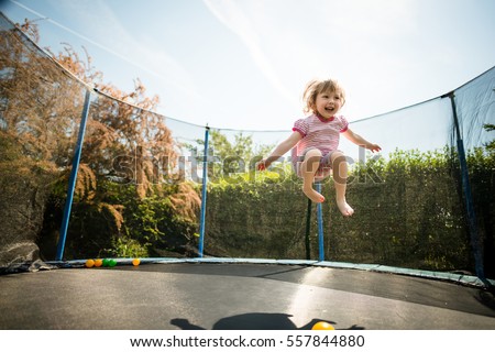 Little child enjoys jumping on trampoline - outside in backyard Royalty-Free Stock Photo #557844880