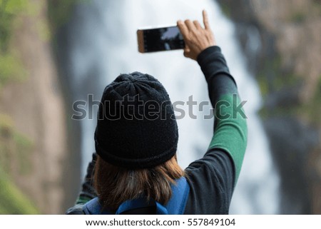 Woman taking photo waterfall in forest by cellphone 