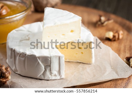 Brie type of cheese. Camembert cheese. Fresh Brie cheese and a slice on a wooden board with nuts, honey and leaves. Italian, French cheese. Royalty-Free Stock Photo #557856214