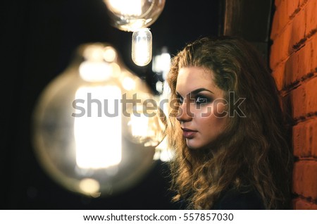 Portrait of a beautiful European girl. A woman stands near a wall surrounded by Edison's light bulbs.
