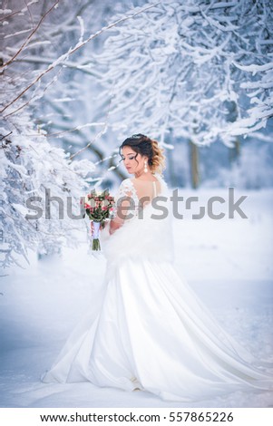 Winter portrait of a bride in a white dress with a bouquet of flowers.