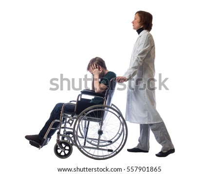 Young distressed boy sitting in a wheelchair holding his head and behind a wheelchair stands a woman in the medical gown on a white background