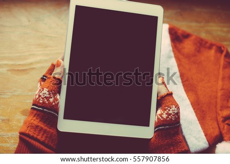 Female Santa Claus holding mobile tablet pc in hands, mockup screen festive Christmas background. Closeup view photo