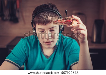 Teenager eating pizza sitting at a laptop. The concept of unhealthy lifestyle.