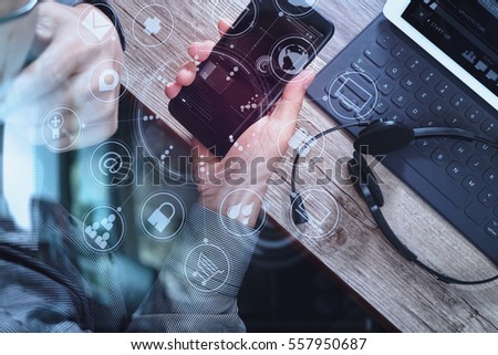 top view of man hand using VOIP headset with digital tablet computer docking keyboard,smart phone, it support, call center and customer service help desk on wooden table,virtual interface icons screen Royalty-Free Stock Photo #557950687